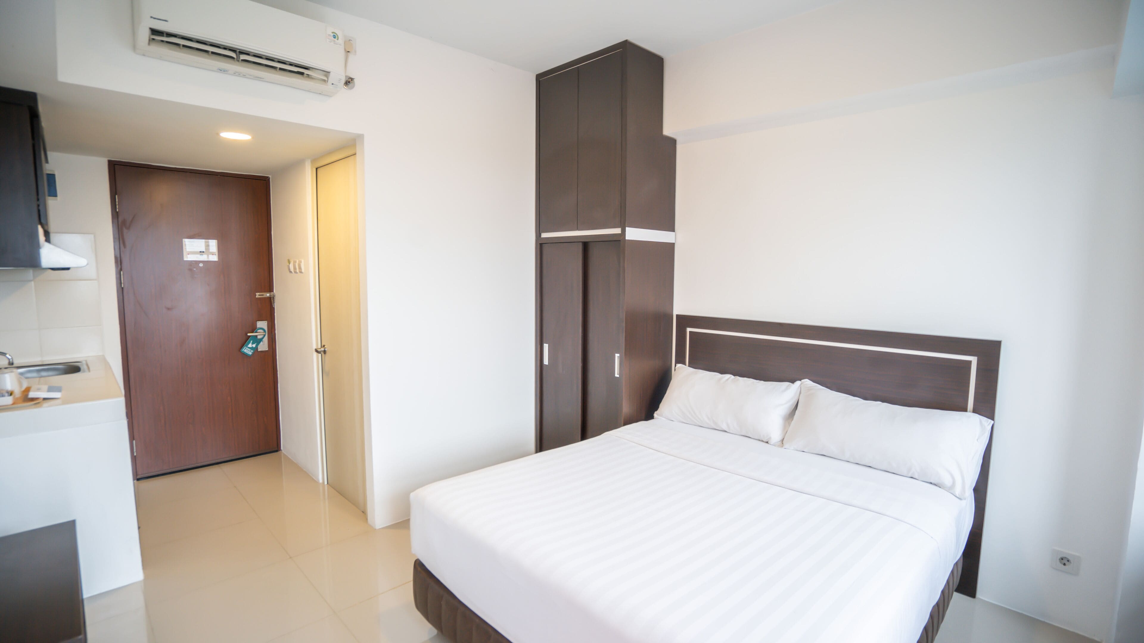 A hotel room with a bed, a wardrobe, a bathroom, and a kitchenette.