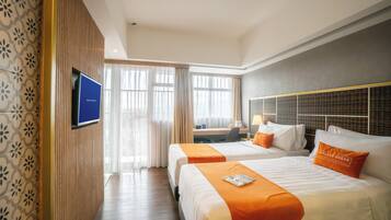 Une chambre d’hôtel avec deux lits, une télévision, un bureau et une vue sur la ville grâce à de grandes fenêtres.