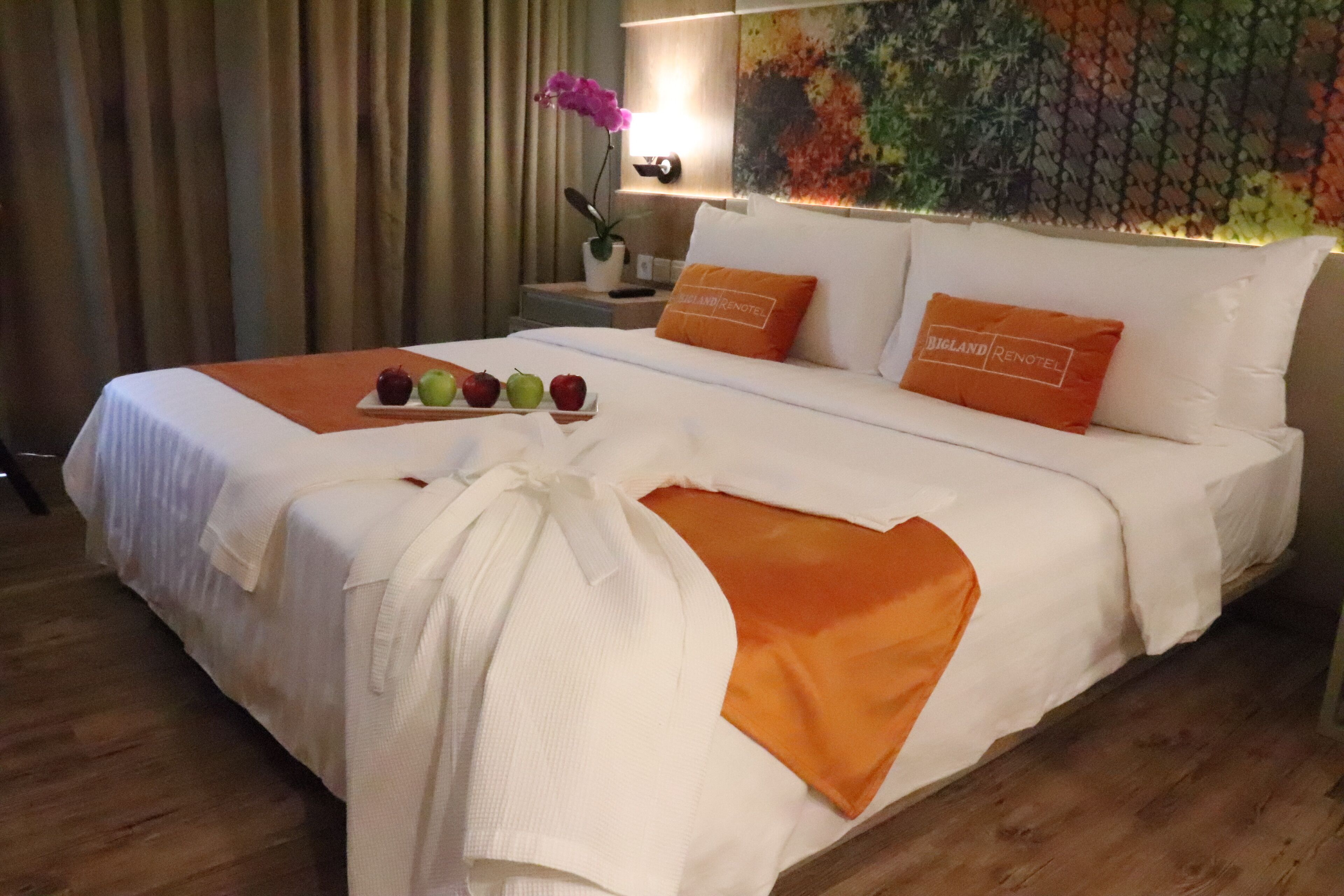 A hotel room with a neatly made bed, a tray of fruit, and a decorative pillow with the hotel name.