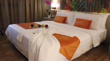 A hotel room with a neatly made bed, a tray of fruit, and a decorative pillow with the hotel name.