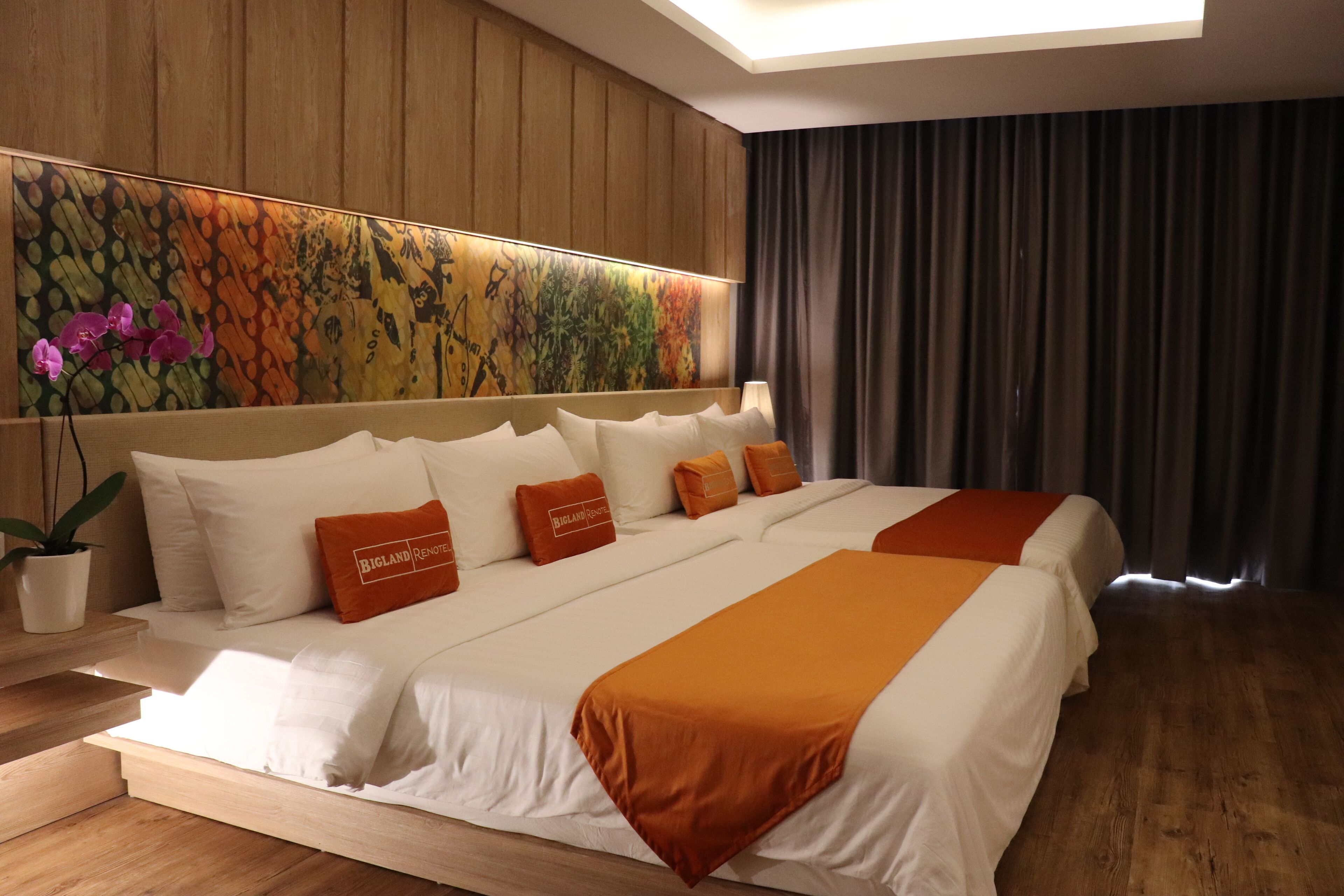A hotel room with a large bed, a headboard with a floral mural, a potted plant, and a view of the outdoors.