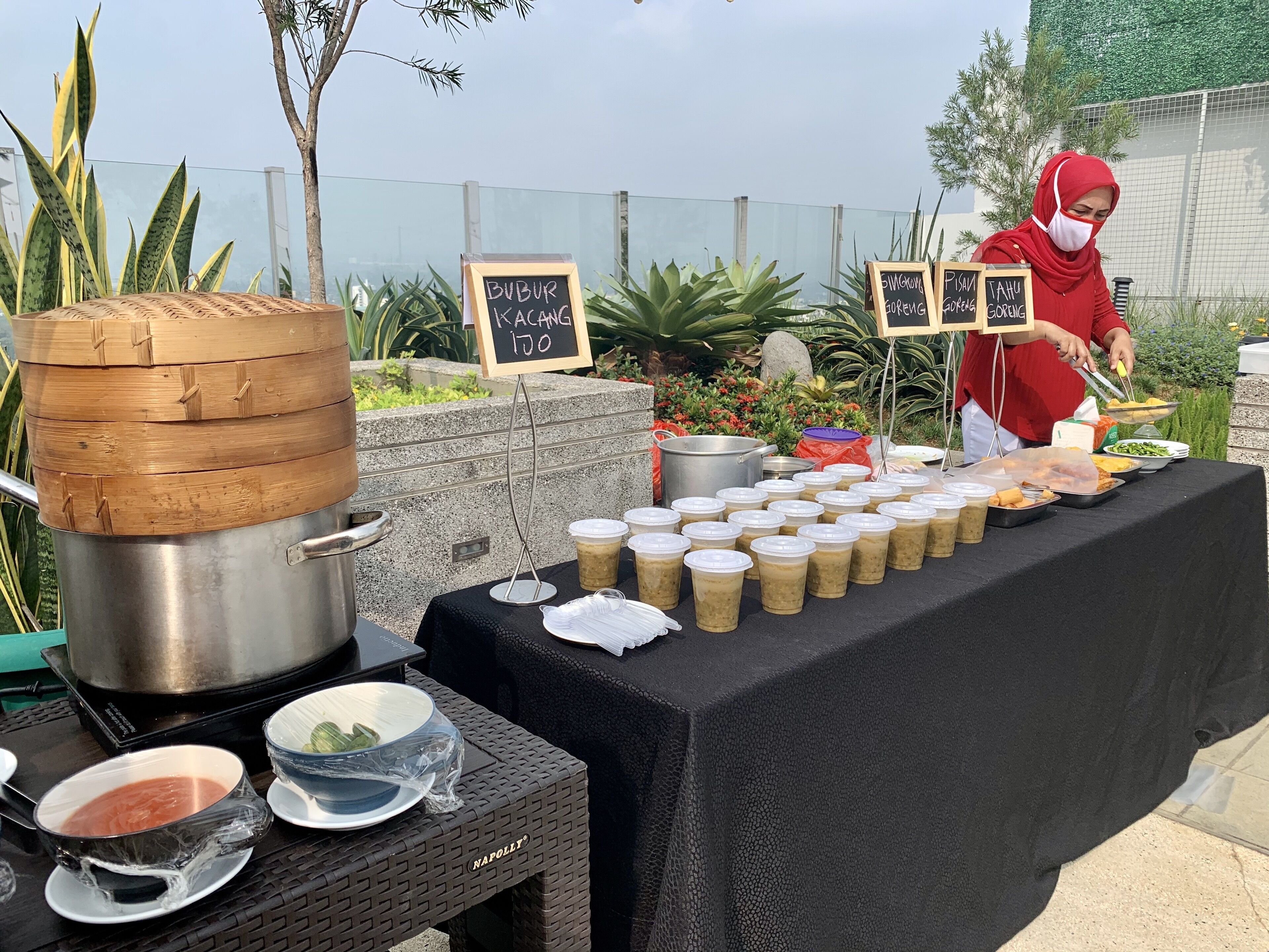 A food stall with a variety of dishes and drinks, a large pot, and a person serving food.