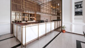 A modern bar area with a long counter, glassware, and a potted plant. - Bigland Bogor Hotel Powered by Archipelago (Bogor)