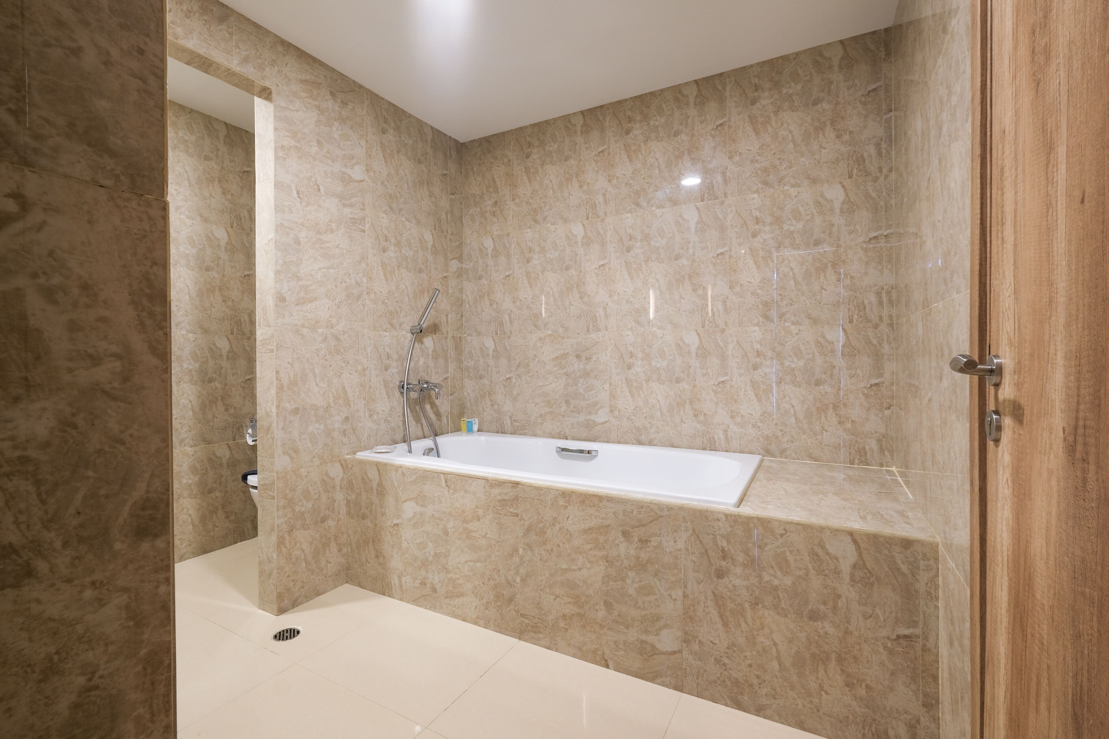 Un baño moderno con una bañera independiente, paredes de mármol y una puerta de madera.
