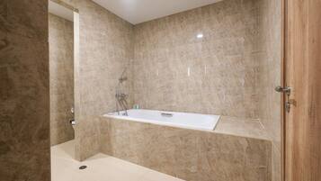 Un baño moderno con una bañera independiente, paredes de mármol y una puerta de madera.