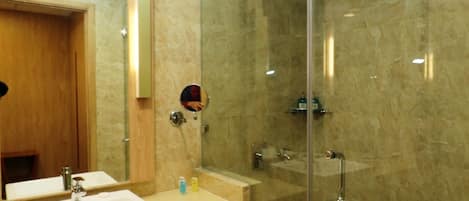 A modern bathroom with a glass-enclosed shower, a wooden vanity with a mirror, and a shelf with rolled towels.
