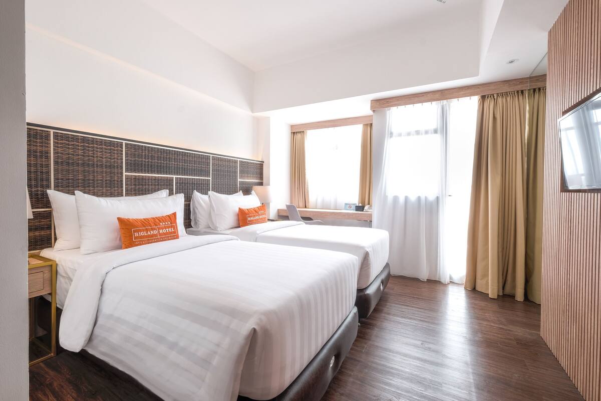 A hotel room with two beds, a large window, and a TV on the wall.