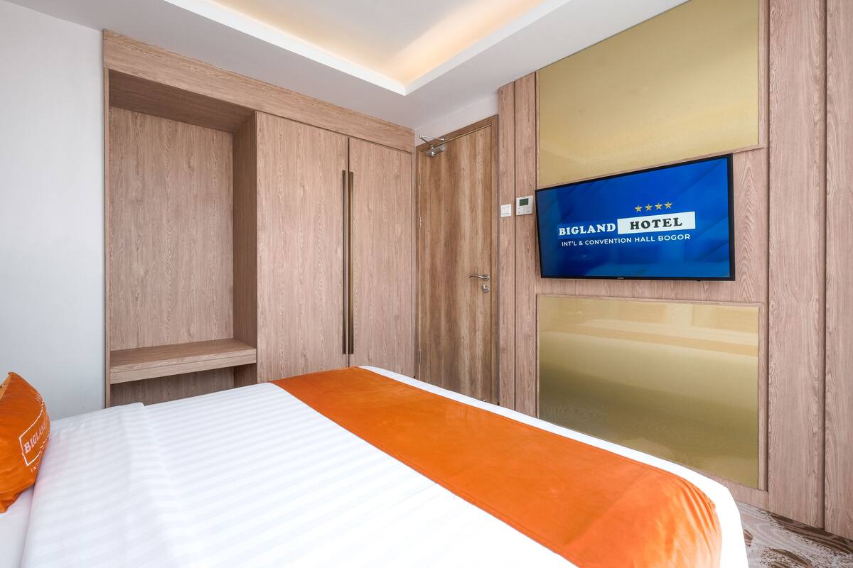A hotel room with a bed, a television mounted on the wall, and wooden wardrobes.