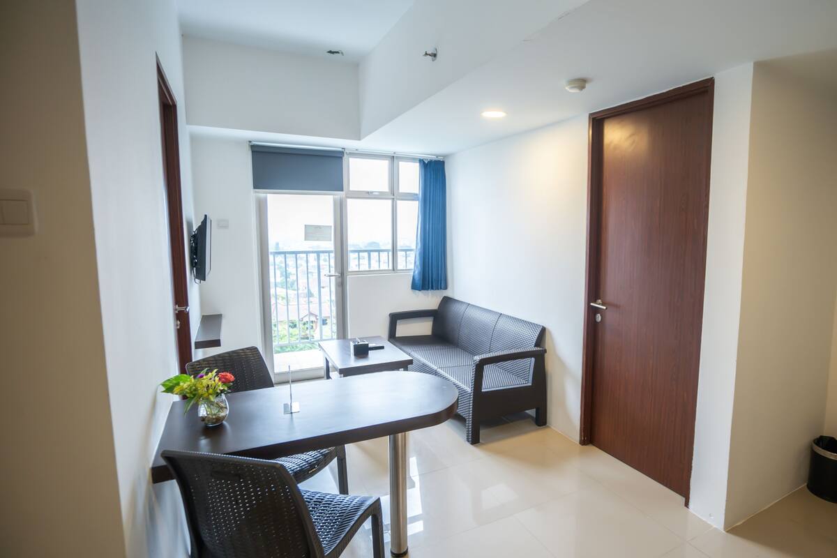A compact living space with a dining area, a sofa, a small table, and a door leading to an outdoor balcony.