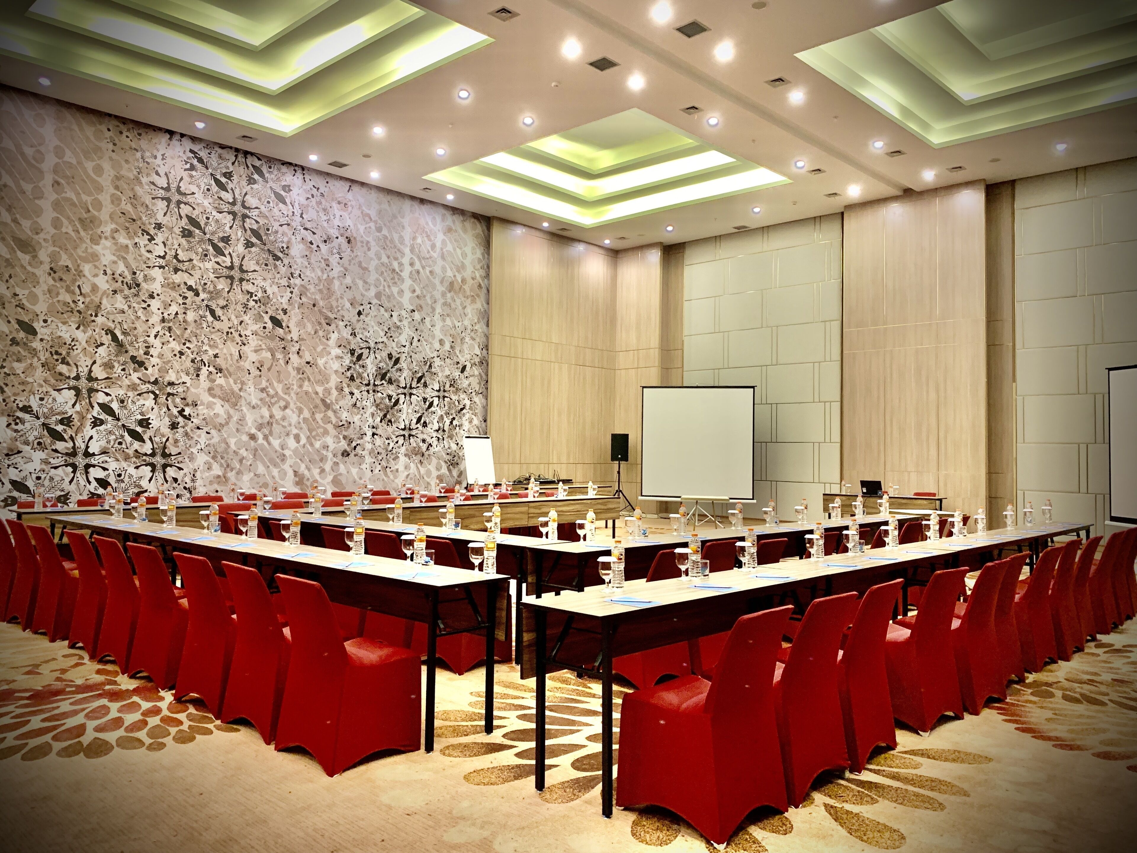 A conference room with a long table, red chairs, a whiteboard, and a projector screen.