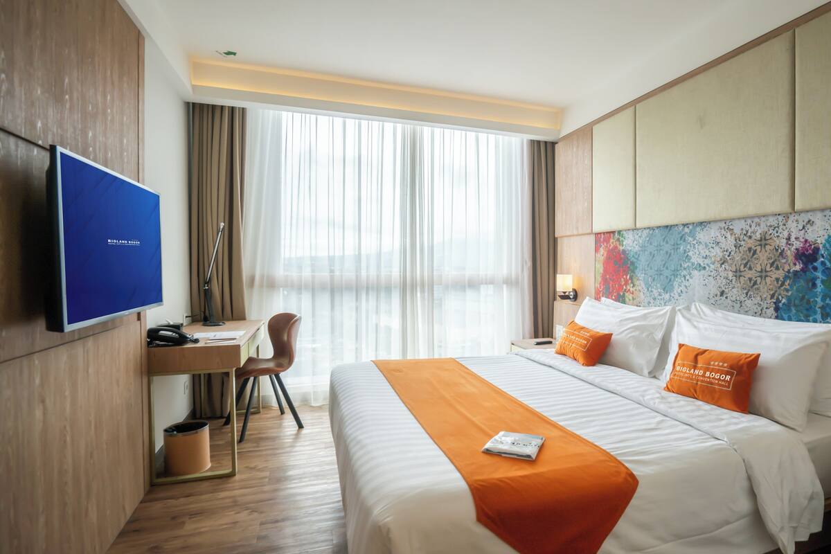 A hotel room with a bed, desk, chair, and a TV.