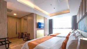 A hotel room with a large bed, a TV mounted on the wall, a desk with chairs, and a large window with curtains. - Bigland Bogor Hotel Powered by Archipelago (Bogor)