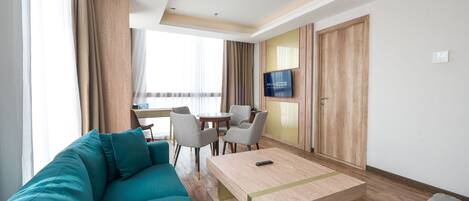A modern hotel room with a teal sofa, a wooden coffee table, and a TV mounted on the wall.