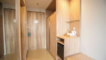 Un pasillo con puertas de madera, una pequeña cocina americana con cafetera y un estante de vidrio.