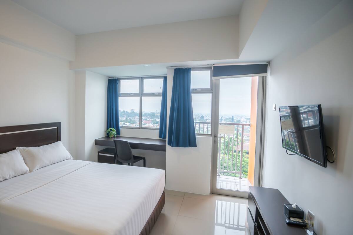 A hotel room with a bed, a desk, a chair, a TV, and a balcony with a view.