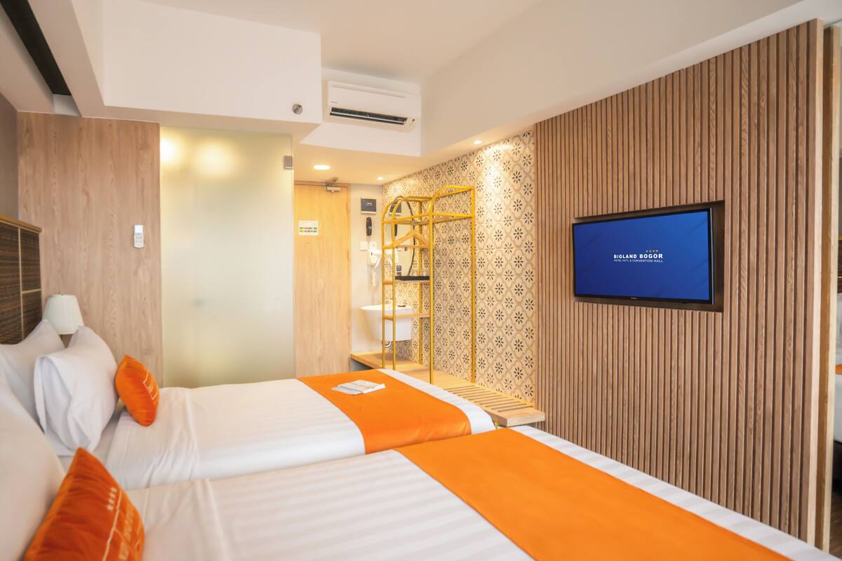 A hotel room with two beds, a television, and a mirror.