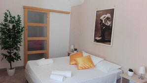 Ein Hotelzimmer mit Bett, einer Topfpflanze, einem Gemälde und einer Schiebetür.