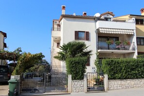 Un immeuble résidentiel à plusieurs étages, doté de balcons, d’un mur en pierre et d’un portail en métal.
