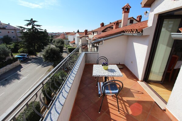 Un balcon avec une table et des chaises, donnant sur la rue et les maisons voisines.