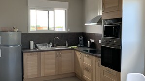A modern kitchen with wooden cabinets, a stainless steel refrigerator, a microwave, and a stove. There is a window providing natural light and a sink with a faucet.