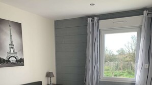 A bedroom with a bed, a nightstand, a chair, a window with curtains, and a radiator.
