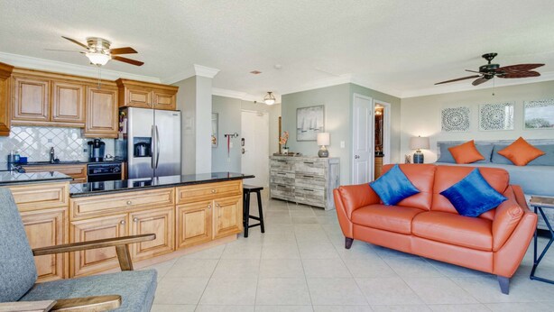 A spacious living area with a kitchen, a leather sofa with blue cushions, and a dining area.