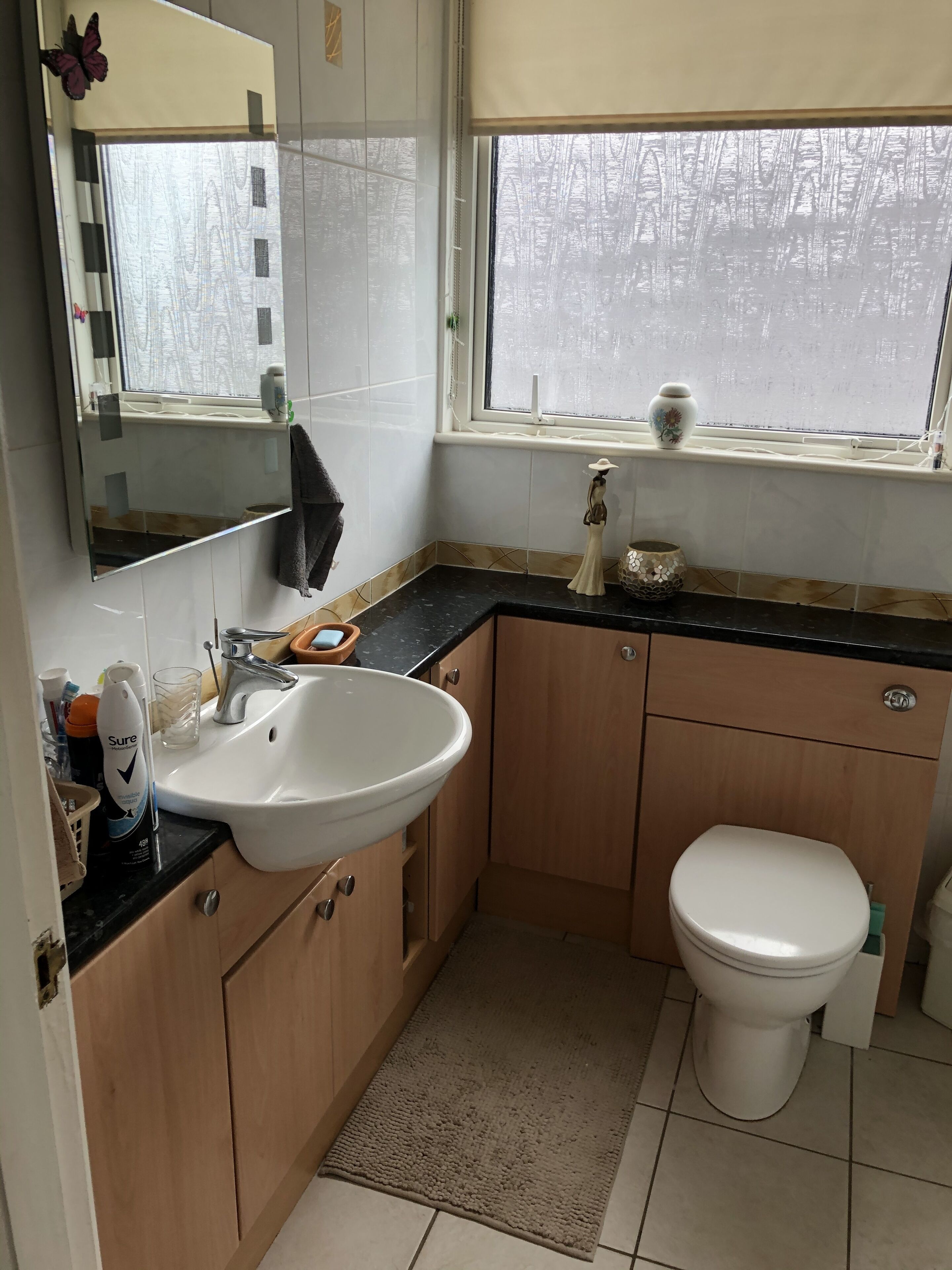 Ein Badezimmer mit einem weißen Waschbecken, Holzschränken, einer Toilette, einem Spiegel und einem Fenster mit Blick auf Bäume.