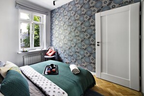 A bedroom with a bed, a window, a radiator, a chair, and a door. - P&O Apartments Siewierska (Warsaw)