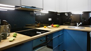 A modern kitchen with a black stovetop, wooden countertop, and blue cabinets. - P&O Apartments Siewierska (Warsaw)