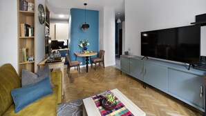 A modern living room with a sofa, coffee table, and a television. There is a dining area with a table and chairs. - P&O Apartments Siewierska (Warsaw)