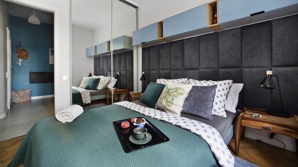 A modern hotel room with a large bed, a small desk, and a sliding door leading to another room. - P&O Apartments Siewierska (Warsaw)