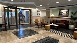 Un vestíbulo con piso de mármol, un mostrador de recepción, un sofá, dos sillones, una mesa de centro y una planta en maceta.