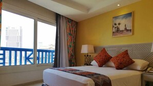 Habitación de hotel con una cama grande, una mesita de noche, una lámpara y una ventana con vistas a edificios.
