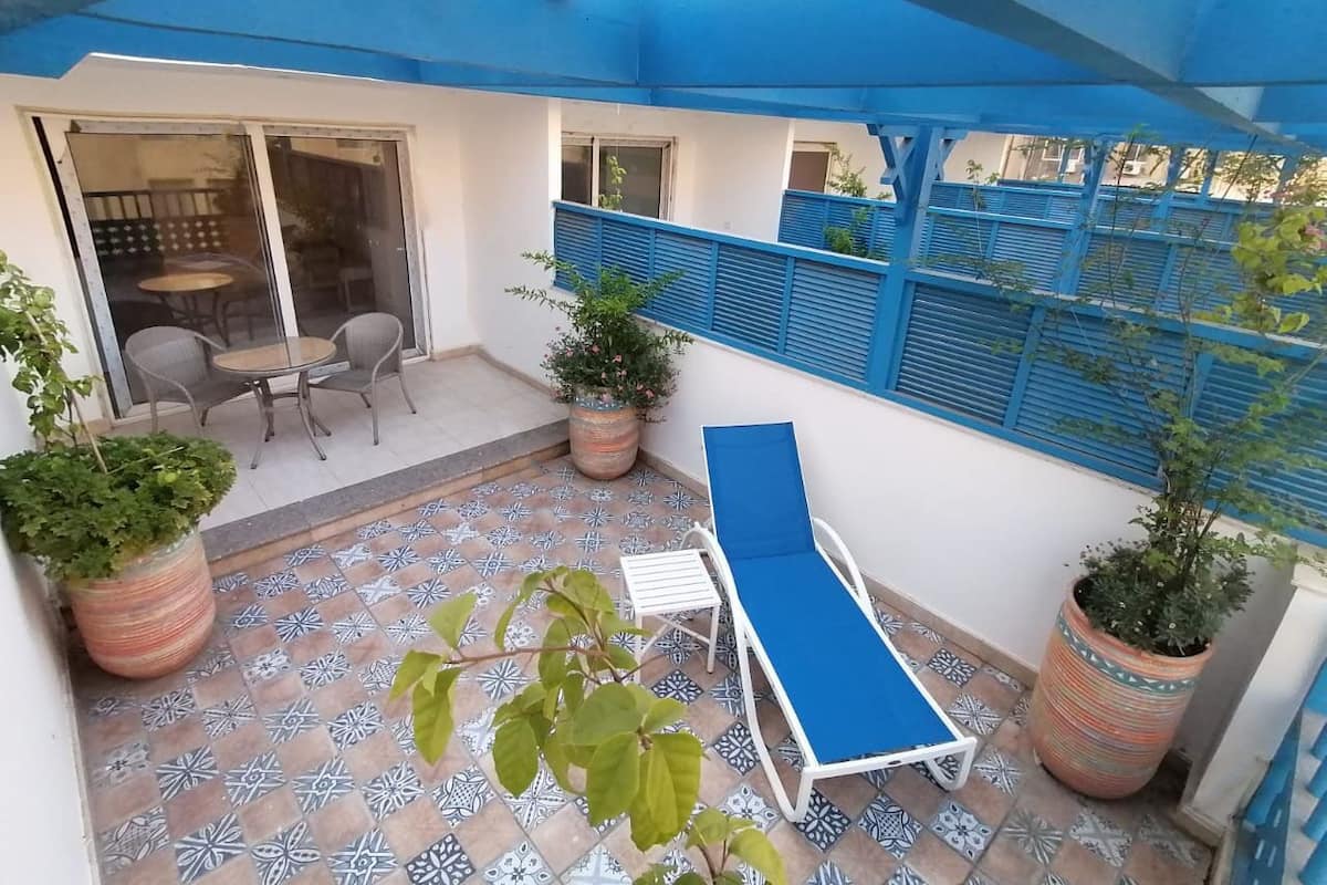 A covered patio with a blue ceiling, a white lounge chair, and potted plants.