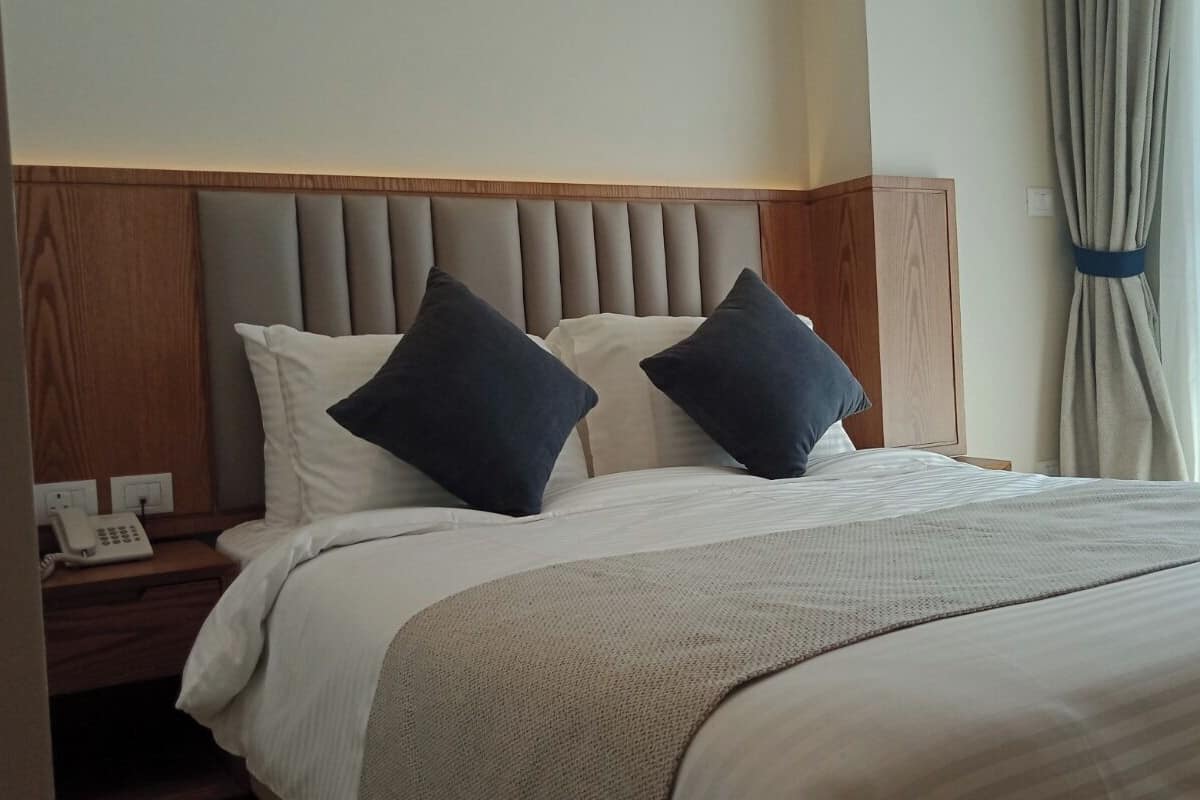 A hotel room with a bed, two pillows, a nightstand with a phone, and a curtain.