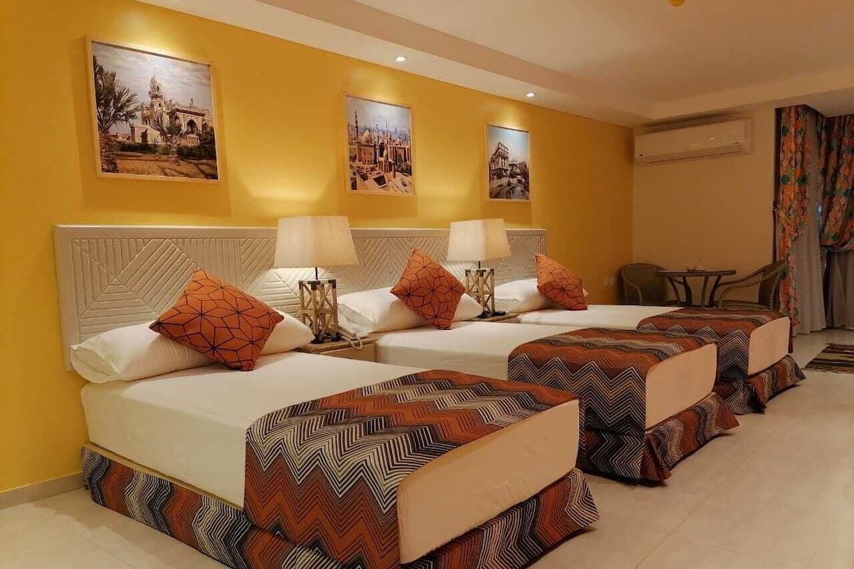 A hotel room with two beds, each with patterned bedding and pillows, a white headboard, and wall-mounted air conditioning.