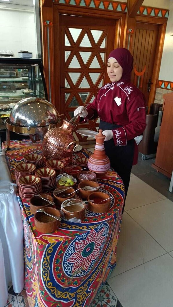 A person serving food from a table with traditional pottery and colorful tablecloth. - Al Madiafa (Cairo)