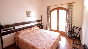 Ein Schlafzimmer mit einem Bett, einem Holzkopfende, einem Nachttisch, einem Sessel und einem Fenster mit Vorhängen.