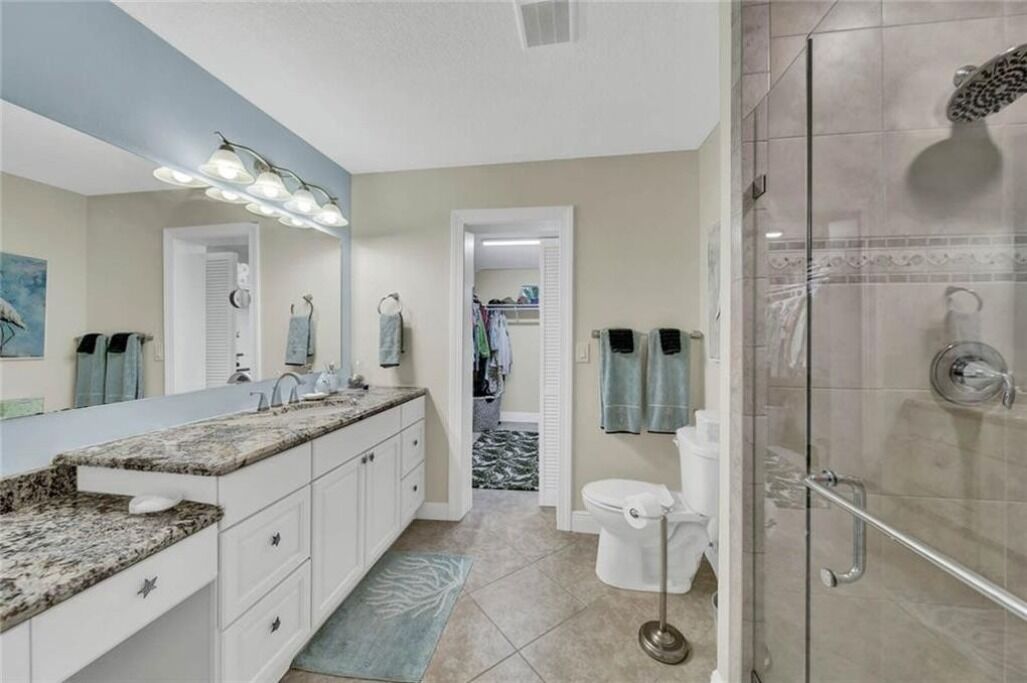 Une salle de bain moderne avec un lavabo sur un plan de travail en granit, une douche à parois de verre et un dressing ouvert, visible à travers une porte.