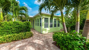 A green building with a paved walkway, surrounded by lush greenery and palm trees. - FANTASY ISLAND LIFE (Jensen Beach)