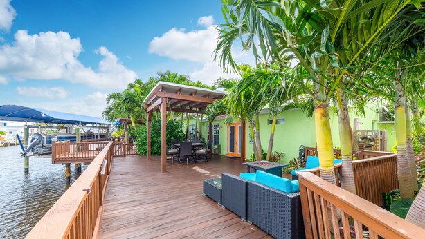 A wooden deck with outdoor furniture, a covered seating area, and a view of the water. - FANTASY ISLAND LIFE (Jensen Beach)