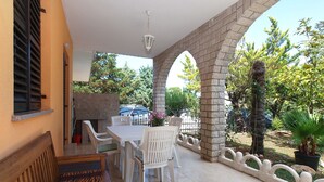 An outdoor patio with a table and chairs, a stone archway, and a view of the surrounding garden and trees. - Apartment 2039/31767 (Istria - Banjole), 300m from the beach (Banjole)