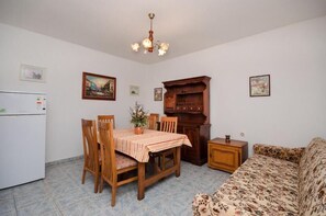 A compact living space with a dining table, chairs, a sofa, a wooden cabinet, and a refrigerator.