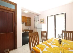 Un comedor con una mesa cubierta con mantel amarillo floreado, sillas de madera y un pequeño florero con flores.