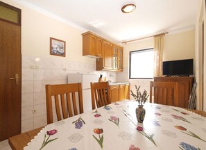 Une cuisine avec des meubles de rangement en bois, un réfrigérateur, une table à manger recouverte d’une nappe à motifs floraux et un vase rempli de fleurs.