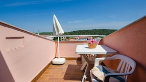 A small outdoor balcony with a table and chairs, a white umbrella, and a view of a green hillside. - Apartment 2039/31774 (Istria - Banjole), 300m from the beach (Banjole)