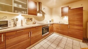 A modern kitchen with wooden cabinets, a stainless steel range hood, and a tiled floor.