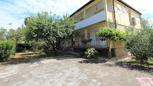 Um edifício de dois andares com fachada amarela, uma varanda com grades e um pátio pavimentado com azulejos hexagonais.