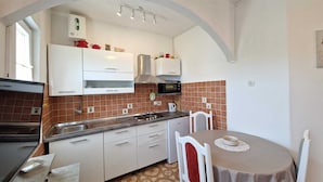 Uma cozinha compacta com armários brancos, micro-ondas, fogão a gás e uma área de refeições com mesa e cadeiras.