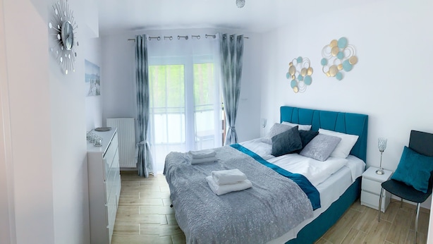 Un dormitorio moderno con una cama grande, una mesita de noche, una silla y una ventana con cortinas.